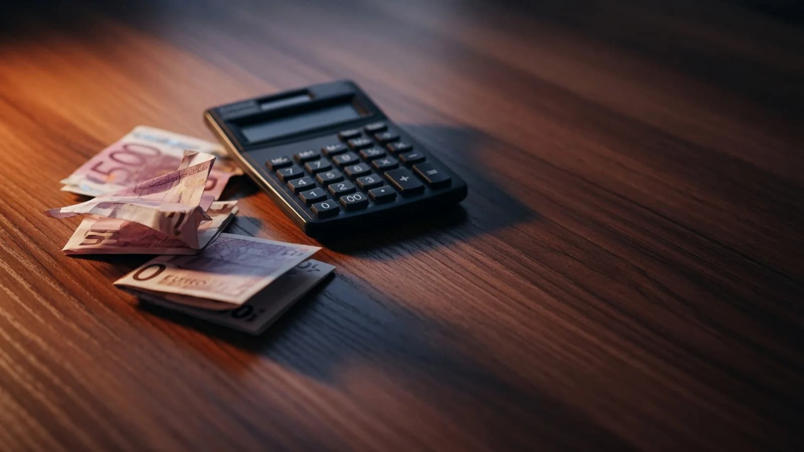 Billetes de euro y una calculadora sobre una mesa de madera